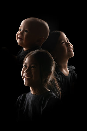 A baby and two young girls are gazing upwards, their expressions filled with wonder and curiosity in the darknessの写真素材