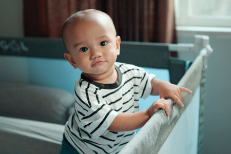 A playful and curious baby leans over the crib, showcasing their cuteness and innocence