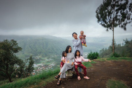 A cheerful family is joyfully posing for a photo on the peak of a scenic mountain, surrounded by beautiful nature and clear skiesの写真素材