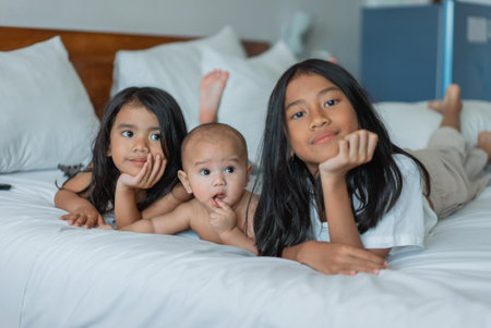 Three adorable and lively kids are joyfully enjoying their playful moments on a cozy bedの写真素材