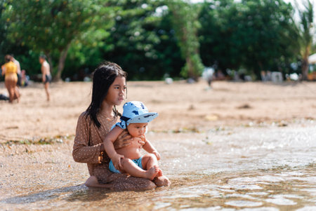 A woman is gently kneeling in the water, cradling a baby in her arms, creating a serene and intimate moment in natureの写真素材