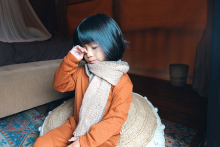 A young child in a cozy outfit and scarf sits indoors, enjoying a peaceful moment