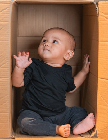 A delightful moment of a baby sitting in a cardboard box, looking around curiously.の写真素材
