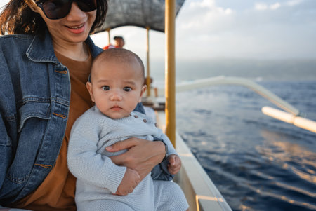 A woman is lovingly holding a baby on a small boat as they both enjoy their time together out in the vast ocean watersの写真素材