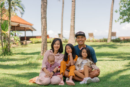 A happy family is sitting together on the lush green grass in a beautiful park on a pleasant day enjoying the lovely weatherの写真素材