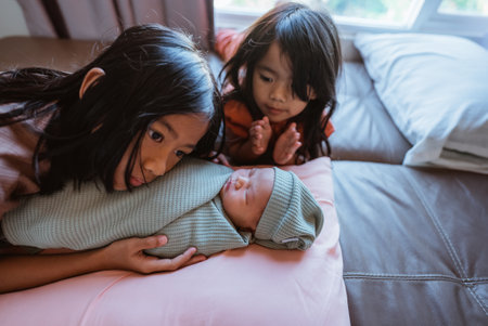 Siblings gaze lovingly at their adorable newborn brother on the couch, sharing a sweet momentの写真素材