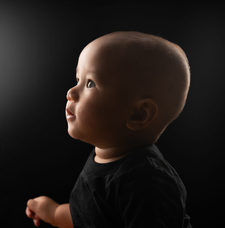 A contemplative baby quietly observing a gentle, soft light within a dimly lit settingの写真素材