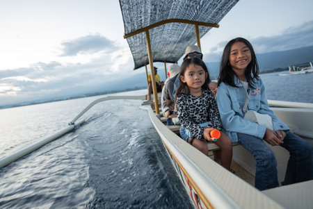 Two young girls are happily sitting together on a small boat that gently floats on the vast ocean, enjoying the beautiful scenery around themの写真素材