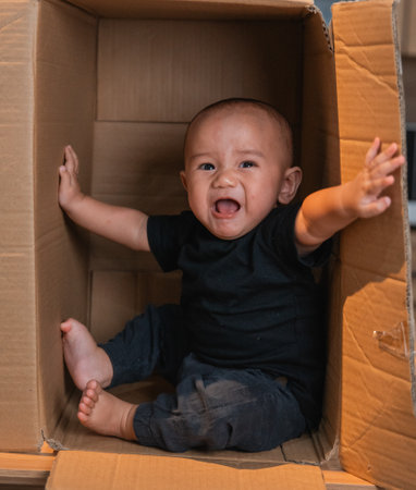 A cheerful baby enjoys playing in a big cardboard box, filled with smiles and laughterの写真素材