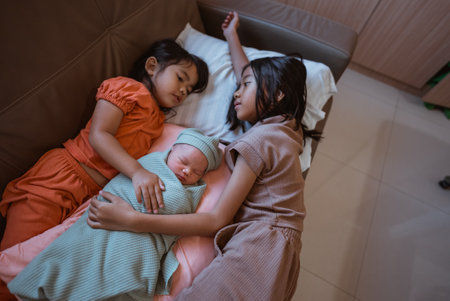 Sisters share a sweet moment with their newborn sibling in a cozy, loving settingの写真素材