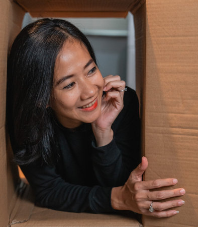 A joyful woman smiles while peeking out from a cardboard box, evoking positivity