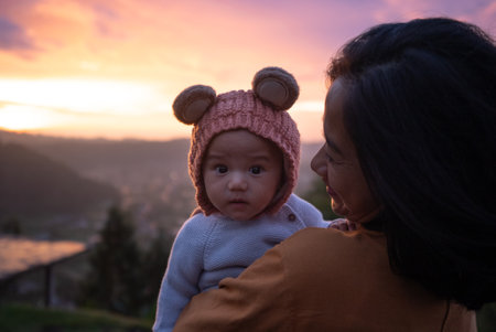 A woman is gently holding a small baby who is adorably wearing a cute teddy bear hat that adds to the joy of the momentの写真素材