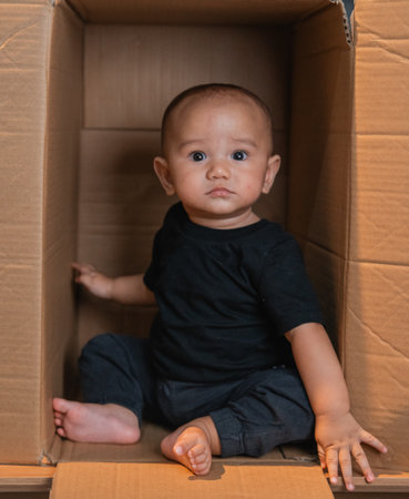 A cute baby explores a cardboard box, displaying curiosity and innocence in their actionsの写真素材