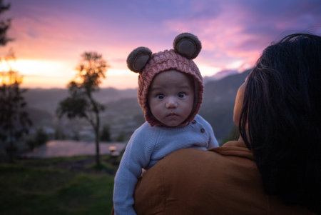 A woman is gently holding a small baby who is wearing an adorable hat that has cute little ears sticking out of itの写真素材