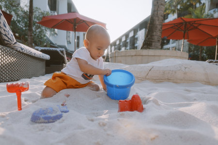 A cheerful child enjoys a sunny day playing in the warm sand with vibrant toys nearbyの写真素材