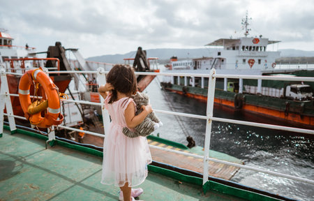 A young girl looks with wonder at various boats sailing by from a ferry on a cloudy dayの写真素材
