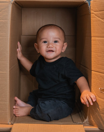 A cheerful baby is seated in a cardboard box, radiating joy and infectious playfulnessの写真素材