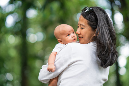 A joyful moment of a mother lovingly holding her adorable baby in a vibrant, green settingの写真素材