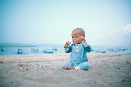 A delightful baby is happily playing on the sandy beach while enjoying a serene ocean viewの写真素材