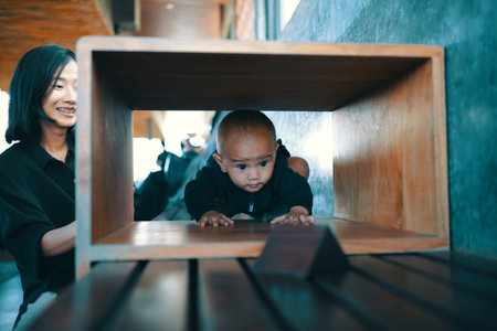 A baby explores a wooden structure while a loving parent watches with a warm smileの写真素材