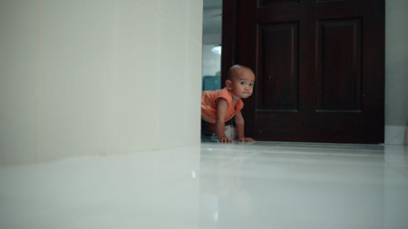 A curious little toddler is happily exploring near an open door in a brightly lit roomの写真素材