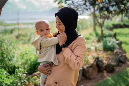 A woman wearing a hijab gracefully holds a tiny baby in her arms, showcasing a beautiful moment of tenderness and love between themの写真素材