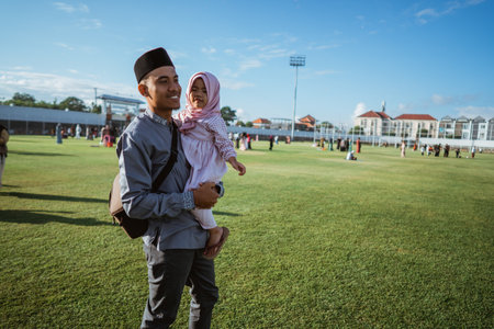 A joyful and loving father carries his cheerful daughter in a vibrant green park, full of lifeの写真素材