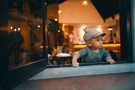 A young child peeks curiously from a caf window, capturing a moment of wonderの写真素材