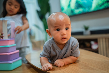 A small baby is energetically crawling on a wooden table while a little girl nearby is happily engaged in playing with her toysの写真素材
