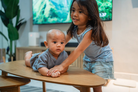 A little girl is happily playing with a baby on a table, enjoying their time together in a joyful and carefree mannerの写真素材