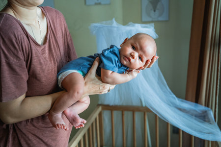 A loving and affectionate parent gently holds a smiling baby close to a cozy cribの写真素材