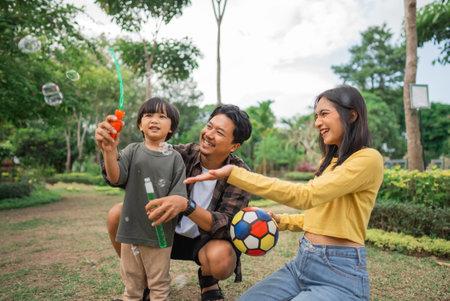 a boy playing bubbles with mom and dad on vacation at the parkの写真素材