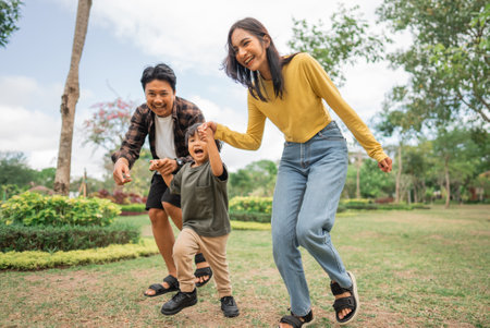 mom and dad take their son for a run while playing together at the parkの写真素材
