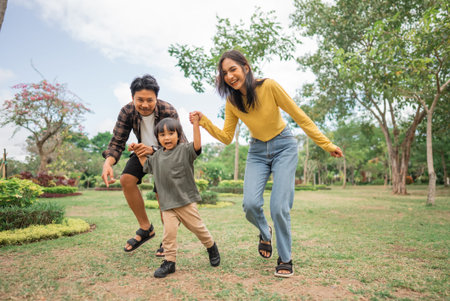 little boy holding hands with mom and dad while running together in the park