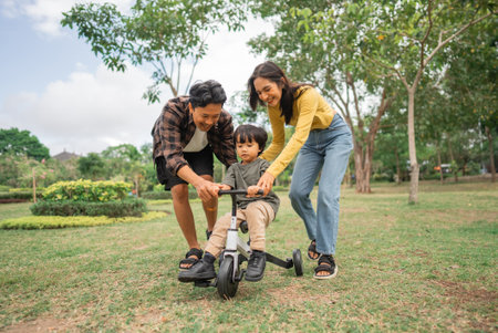 little boy riding a tricycle with mom and dad while playing in the parkの写真素材