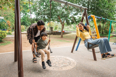 little boy with dad on the swing and mom playing in the parkの写真素材