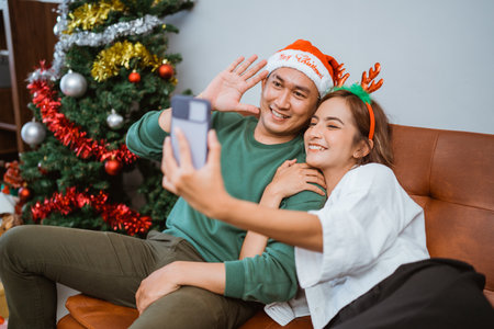 A happy couple taking a festive selfie by their beautifully decorated Christmas treeの写真素材