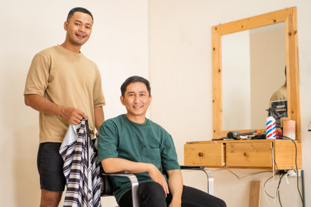 A man is comfortably seated in a chair while a barber skillfully works on giving him a haircut that he desires, focusing on style and precisionの写真素材