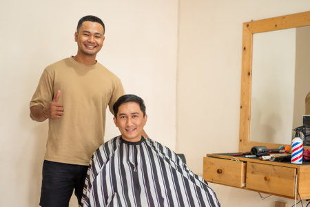 A man is currently getting his hair expertly cut by a professional barber inside a bustling barber shop filled with lively chatterの写真素材