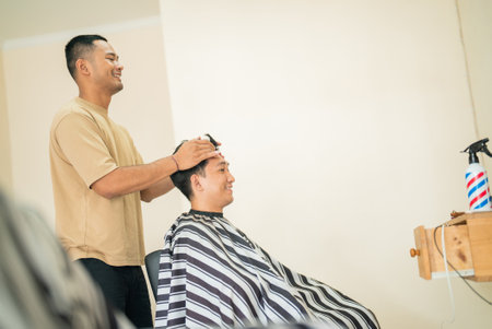 A man is sitting in a barber shop, receiving a haircut from an experienced barber, who is skillfully shaping his hairの写真素材