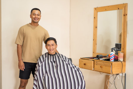 A man is currently in the process of getting his hair cut by a skilled barber in a barber shop that is bustling with activityの写真素材