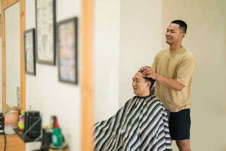 A man is currently getting his hair expertly cut by a skilled barber in a bustling barber shop, filled with lively chatter and laughterの写真素材