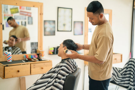 A man is currently in the process of having his hair meticulously cut by a skilled barber in a bustling barber shop, enjoying the experienceの写真素材