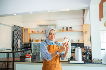 attractive woman in a veil takes a selfie using a cellphone at a coffee shopの写真素材