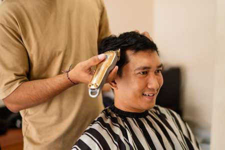 A man is currently seated in a chair, getting his hair cut by a skilled barber who is focused on making him look his bestの写真素材