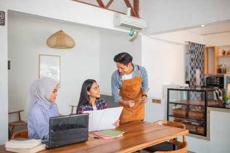 male waiter asks two female customers to order from the menu at a coffee shopの写真素材