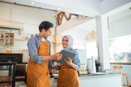 couple of waiters chatting while using a tablet computer together at a coffee shopの写真素材