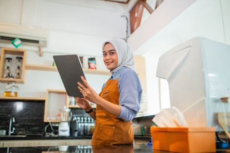 A beautiful Asian woman wearing an apron using a tablet at a coffee cafeの写真素材