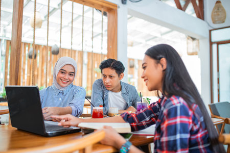 three students sit together using a laptop in a coffee shopの写真素材