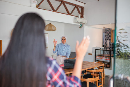 two Asian women meet with a waving gesture in a coffee shopの写真素材